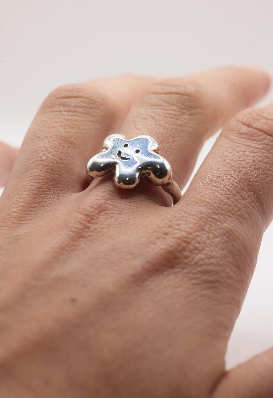 Silver happy face ring on finger.