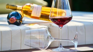 Wine glass on table with bottles outdoors.