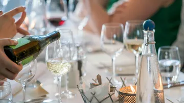 Person schenkt Wein an elegantem Abendtisch ein.
