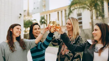 Vier Frauen stoßen im Freien mit Sekt an.