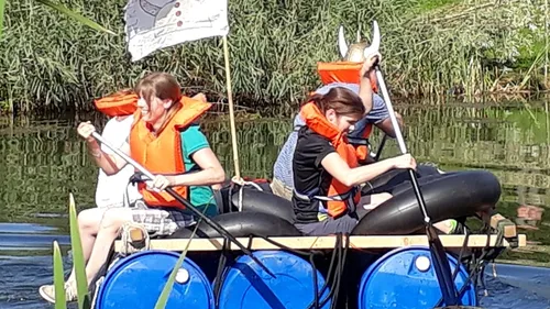 Menschen paddeln auf einem selbstgemachten Floß im Wasser.
