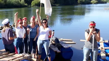 Group celebrates on raft by riverside.