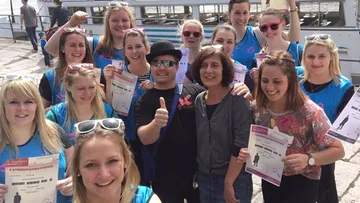 Group of people posing with certificates by a boat.