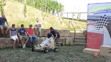 Person im Holzkart wird von einer anderen geschoben, Outdoor-Event.