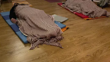 Zwei Personen schlafen auf Matten mit gestreiften Decken.