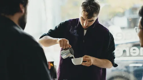 Person pouring drink into cup at cafe.
