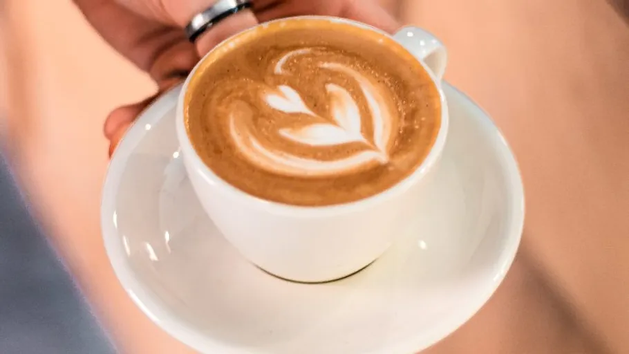 Tasse mit Latte-Art in Hand gehalten.