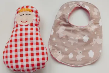 Rot-kariertes Püppchen und Hasen-Lätzchen auf Tisch.
