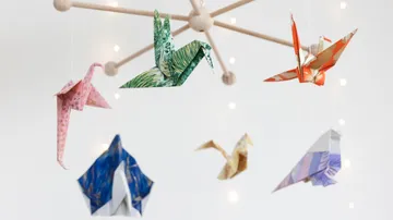 Origami cranes hanging on mobile, string lights background.
