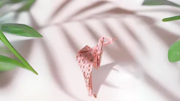 Rosa Origami-Kranich auf weißer Fläche.