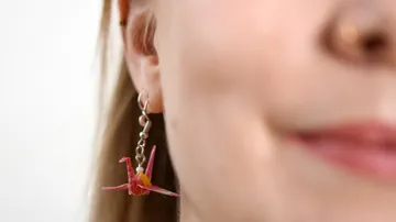 Origami-Ohrring schmückt Ohr einer lächelnden Frau.