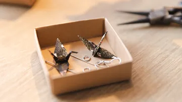 Origami-Vögel und Schmuck in Schachtel auf Tisch.