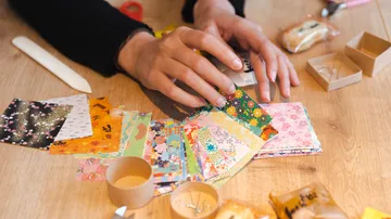 Hände arrangieren buntes Origami-Papier auf Tisch.