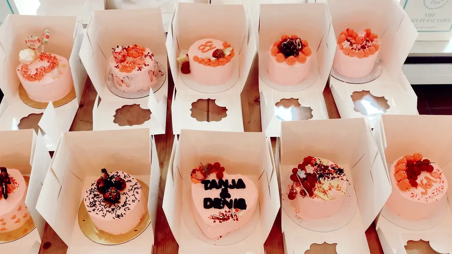 Pink cakes in open white boxes on table.