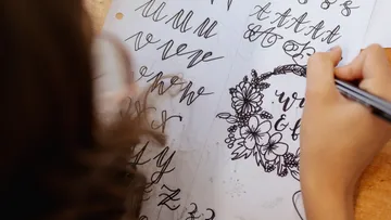 Person übt Kalligrafie mit Stift auf Papier.