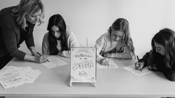 Frauen unterrichten Kalligraphie mit Mädchen am Tisch.