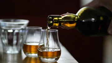 Whiskey being poured into two glasses on table.