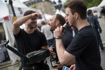 Drei Männer lachen und trinken bei Outdoor-Event.