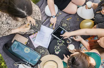 Personen beim Picknick, zeigen auf Tablet.