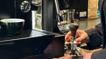 Person tampt Kaffee in einer Espressomaschine.