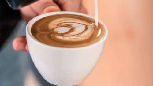 Latte Art wird in eine weiße Tasse gegossen.
