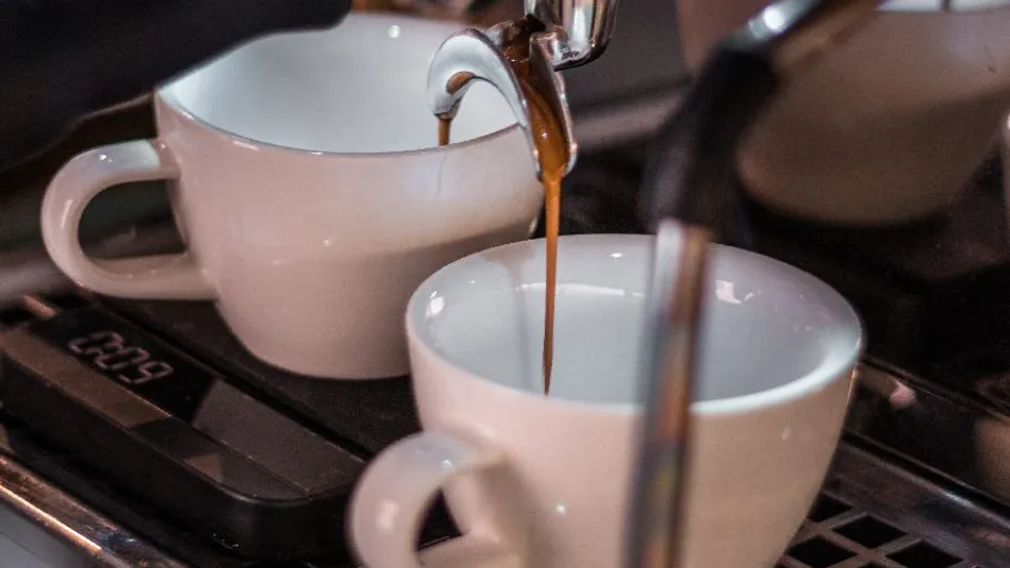 Espresso fließt in zwei weiße Tassen.
