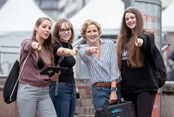 Four women pointing together outdoors.