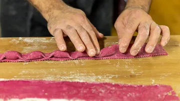 Hände falten rosa Pastateig auf Holzoberfläche.