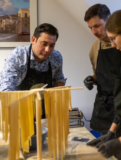 Three people making fresh pasta in kitchen.