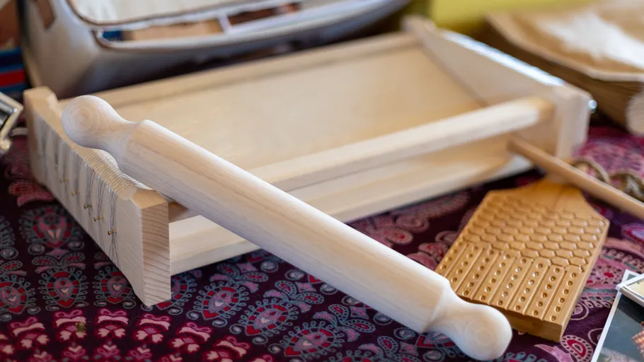 Wooden ravioli press and rolling pin on table.