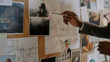 Hand points to photo on evidence board.