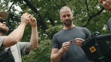 Three men observing a small object outdoors.