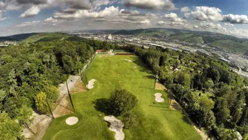 Golf course surrounded by forests and hills.