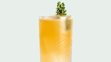 Orangener Cocktail im Glas mit Kräutern.
