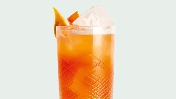 Orange cocktail in glass with ice, orange peel garnish.