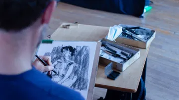 Artist sketching a portrait at a table.