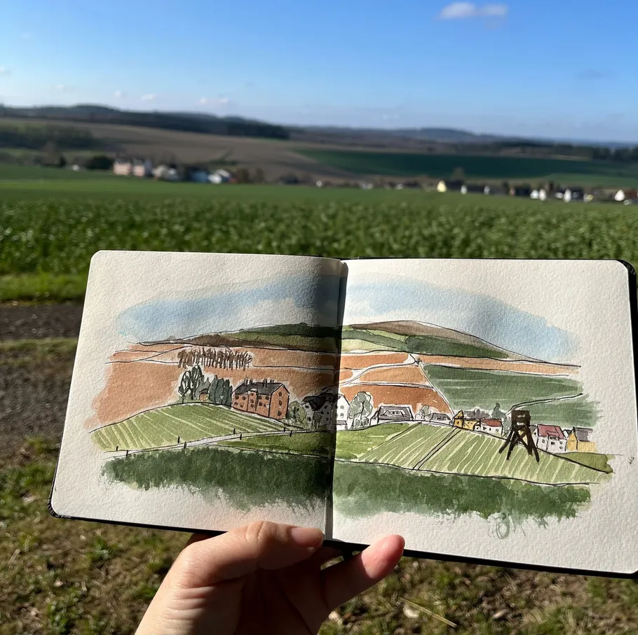 Hand holds sketchbook with landscape drawing.