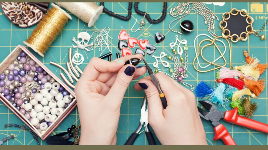 Hands crafting jewelry on a cluttered worktable.