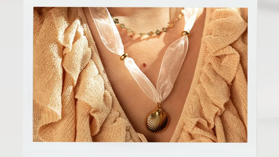 Necklaces worn over ruffled beige top.