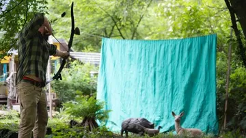 Man practicing archery in a forest setting.