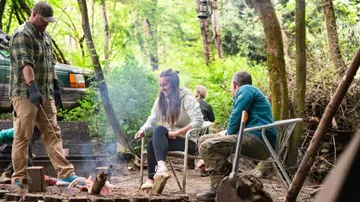 People sitting around campfire in forest.