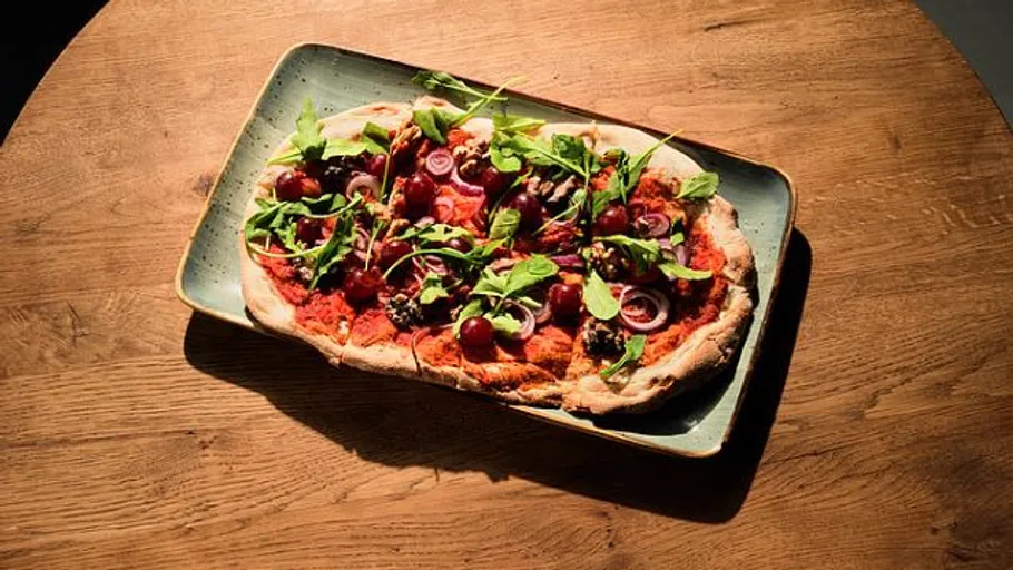 Pizza with greens on wooden table.