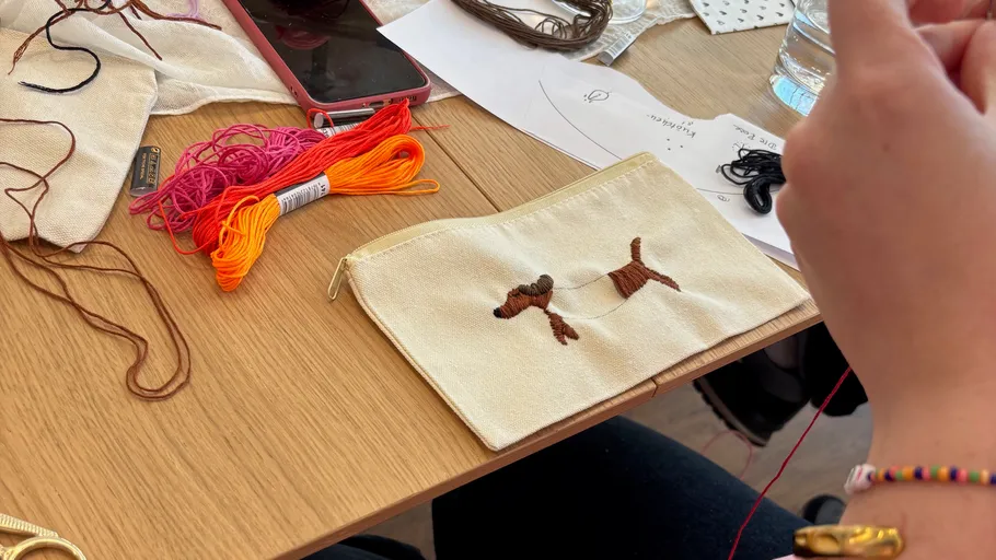 Person embroidering a dog on fabric pouch.