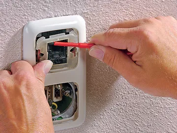 Hände reparieren Steckdose mit einem kleinen Werkzeug.