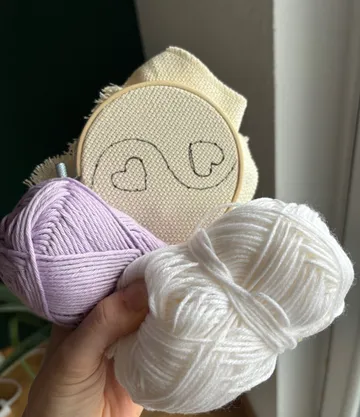 Hand hält Garn und Herz-Stickrahmen.