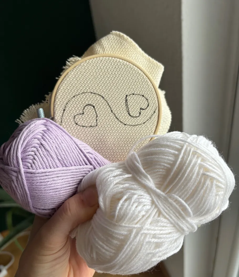 Hand holding yarn and heart embroidery hoop.