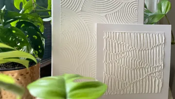 Textured white artwork with plants nearby.