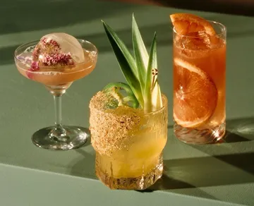Three cocktails with decorative garnishes on table.