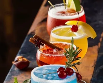 Four colorful cocktails on a wooden table.