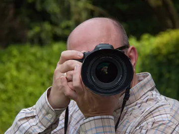 Ein Mann hält eine Kamera und fotografiert vor Hintergrund.
